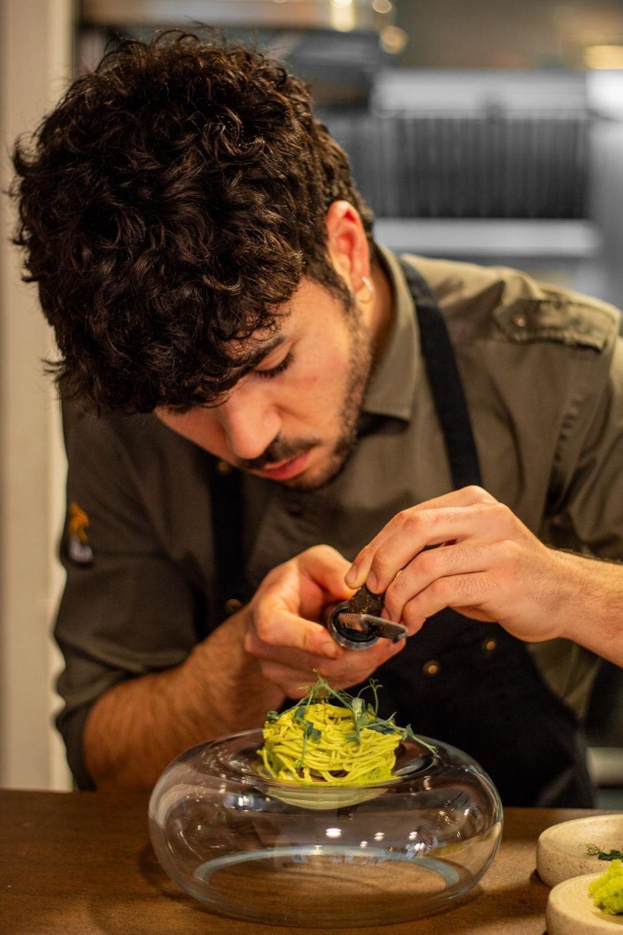 El chef Andrés Rengel rallando trufa sobre un plato de pasta verde